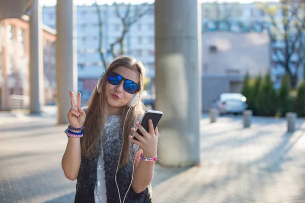 A ten-year-old girl with long hair and sunglasses listens to music from the phone — Stock Photo, Image