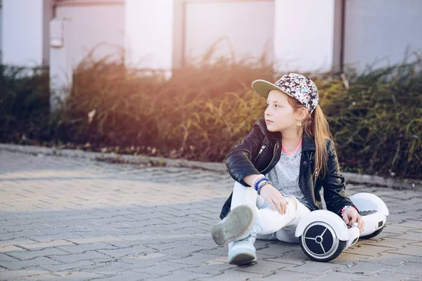 Een 10-jarig meisje met een honkbalpet op de stoep met een hoverboard. — Stockfoto