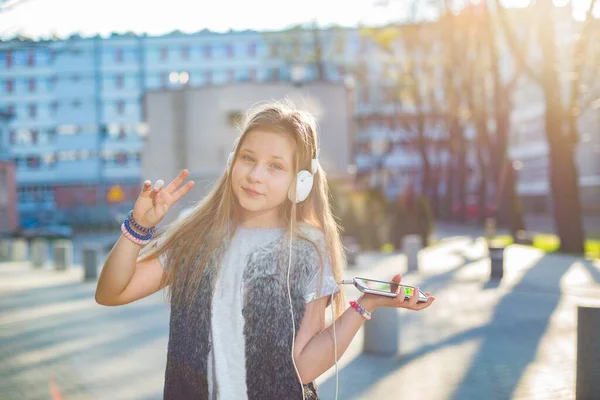 Smiling young girl in headphones listens to music from the phone — Stock Photo, Image