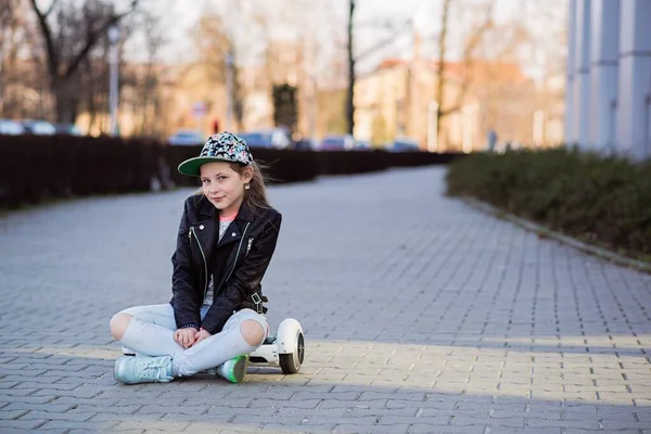 Verlegen jong meisje in een pet is rustend op een hoverboard. — Stockfoto