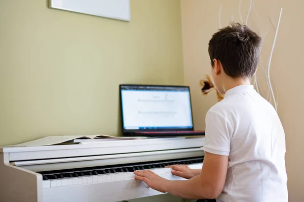 一个12岁的小男孩在一架白色钢琴上弹奏着乐谱 — 图库照片