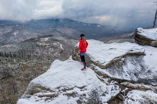 Вид на дрон на атлета бігуна, що стоїть на скелі, милуючись красивими краєвидами на гору . — стокове фото
