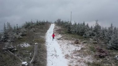 Dişi bir koşucunun kış manzarasında bir dağ yolunda koştuğu İHA videosu.