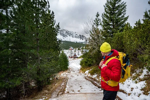 一位穿着红色羽绒服和黄色背包的游客站在山路上看着群山. — 图库照片