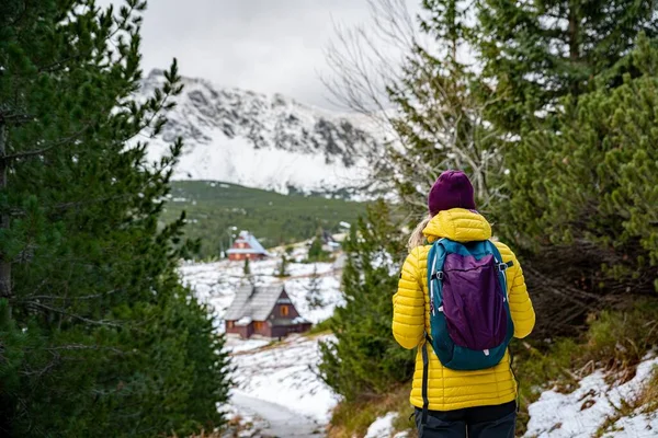 Жінка-туристка в жовтій куртці з рюкзаком стоїть з нею спиною на гірській стежці . — стокове фото