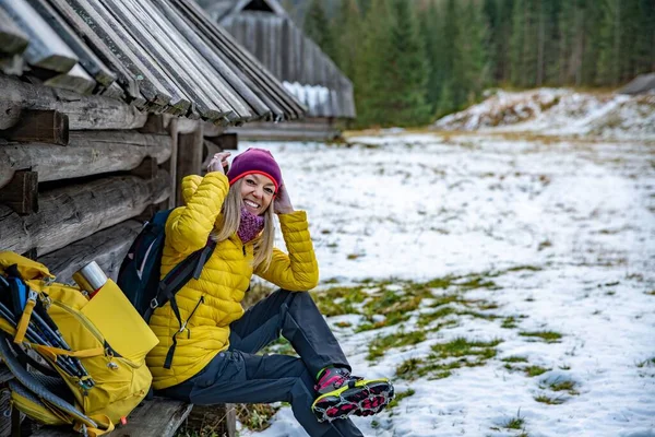 En leende blond turist i gul dunjacka bär kramponger för skor. — Stockfoto