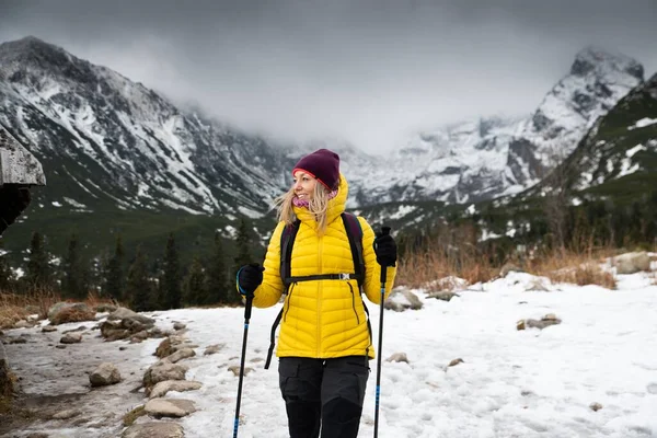 Мандрівник жінка в пуховику пішохідний з пішохідними стовпами на шляху в горах . — стокове фото