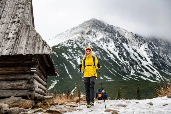 Leende turist kvinna i dunjacka vandring med nordiska gångstavar på spår i vackra berg. — Stockfoto