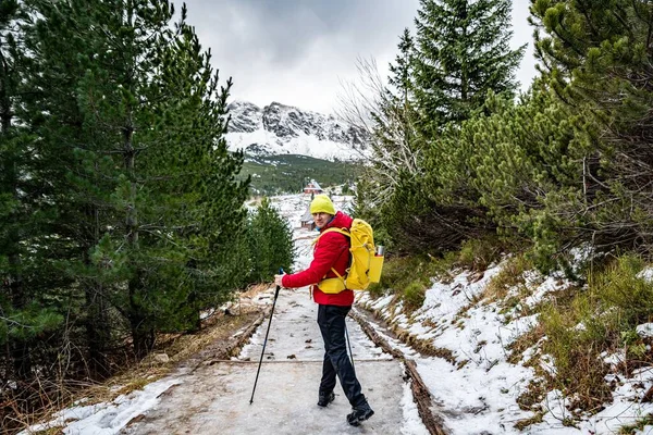 Красивий пішохід у червоній куртці, жовтій чашці та жовтому рюкзаку блукає гірською стежкою зі скандинавськими пішохідними полюсами . — стокове фото