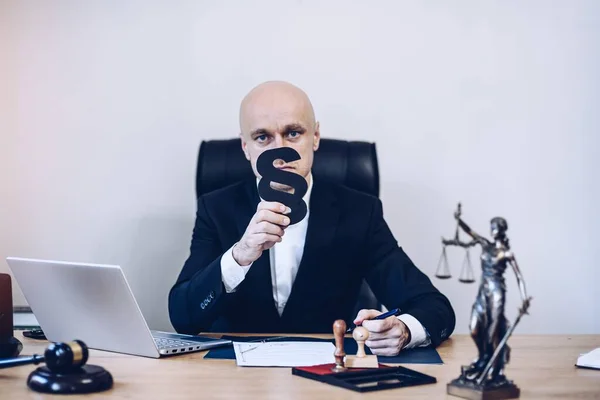 Ein gutaussehender Notar sitzt am Holztisch und hält einen Paragrafen als Zeichen von Recht und Ordnung in der Hand.. — Stockfoto