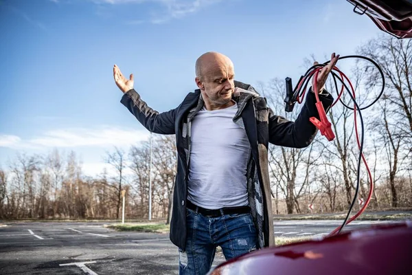 Conductor enojado tratando de arrancar el coche roto con cables de puente —  Fotos de Stock