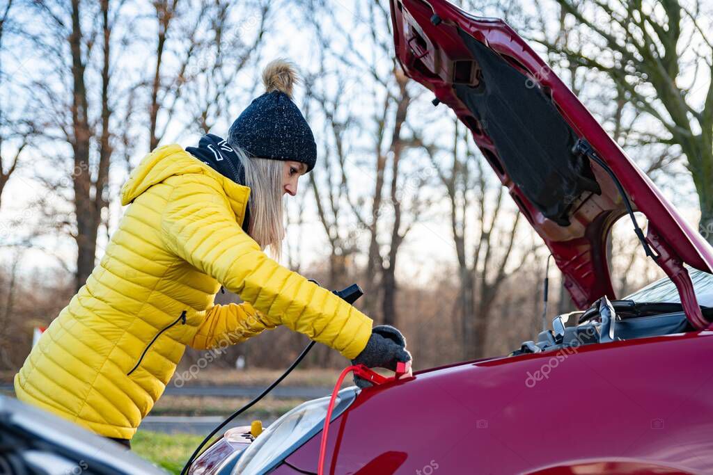 A woman is trying to connect the jumper cables in the car.
