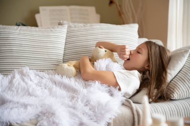 Kız hasta yatıyor, esniyor, elinde bir oyuncak ayı tutuyor..
