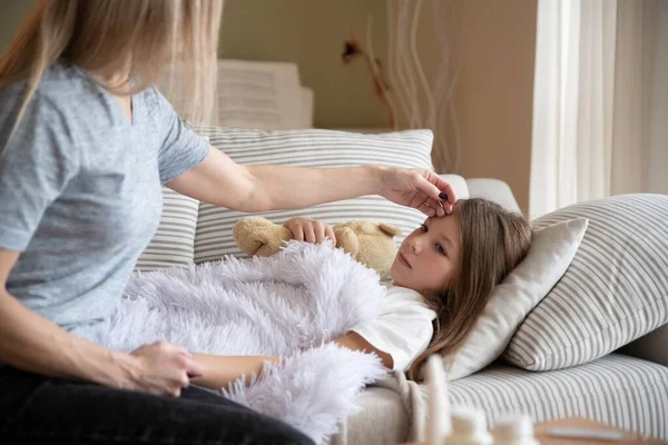 Uma menina doente está deitada debaixo do cobertor. Mãe febre de verificação. — Fotografia de Stock