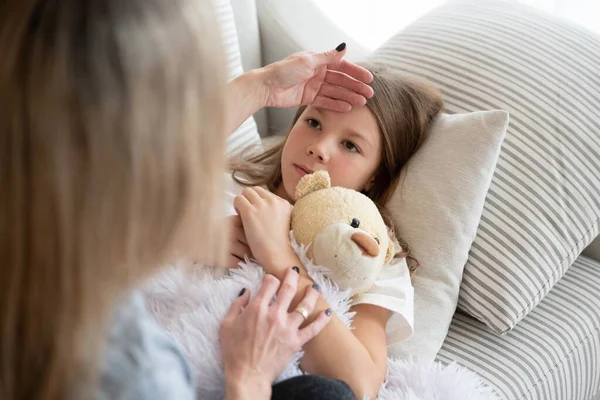 A beteg lány a plüssmackóval fekszik. Anya lázat keres.. — Stock Fotó