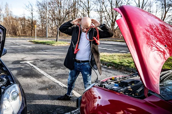 Woedende bestuurder probeert te starten kapotte auto met startkabels. — Stockfoto