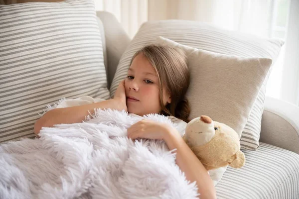 Een ziek bezorgd klein meisje bedekt met deken knuffelt teddybeer. — Stockfoto
