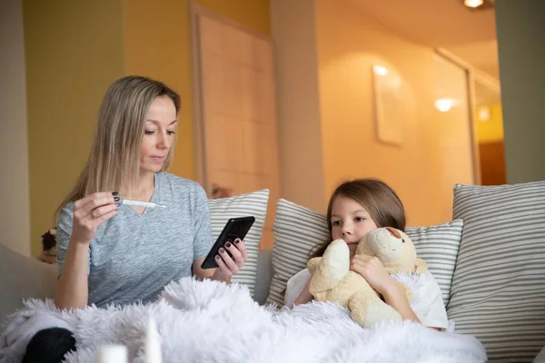 Anne, çocuk sıcaklığını kontrol et ve doktoru aramak için telefonu tut.. — Stok fotoğraf