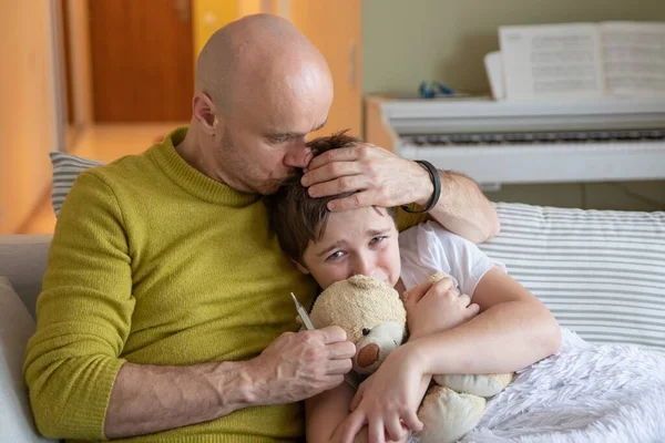 Eenzame vader controleert op koorts. Hij knuffelt en kust zijn zieke zoon.. — Stockfoto