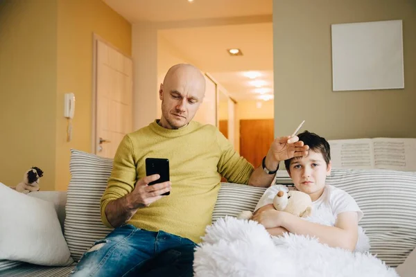 Een alleenstaande vader neemt de temperatuur van zijn zieke zoon en belt de dokter.. — Stockfoto