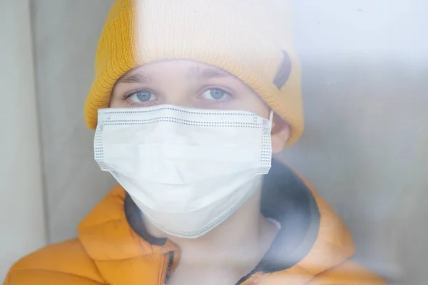 Porträt eines traurigen Jungen, der mit Schutzmaske am Fenster steht. — Stockfoto