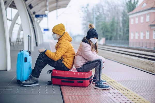 Kinder sitzen auf dem Bahnsteig des Bahnhofs auf Koffern. Es ist verboten, während der Pandemie zu reisen. — Stockfoto