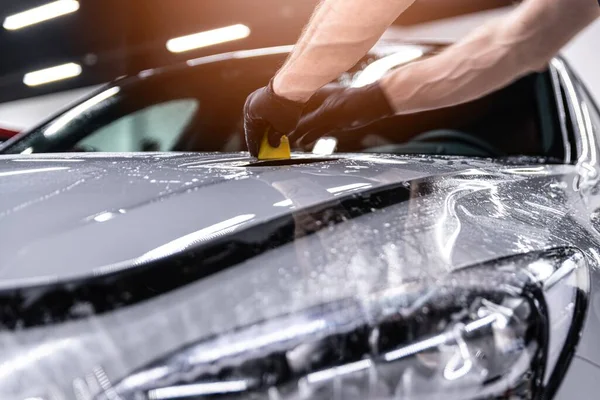 Autodetailaufnahme eines Studiomitarbeiters, der eine Schutzfolie auf die Karosserie aufträgt — Stockfoto