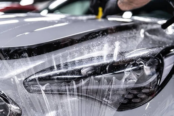 Car detailing studio worker applying protective ppf foil film on car body