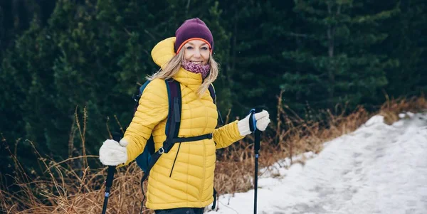 Усміхнений блондин-турист в жовтій куртці на зимовому шляху в горах . — стокове фото