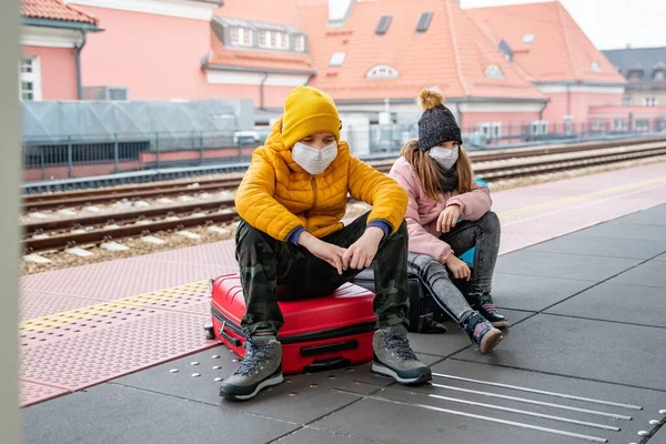 Geschwister tragen Schutzmasken auf einem Bahnhof während einer Pandemie. — Stockfoto