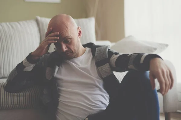 Un hombre deprimido se sienta en el suelo de la sala de estar cubriendo su cara con su mano. — Foto de Stock