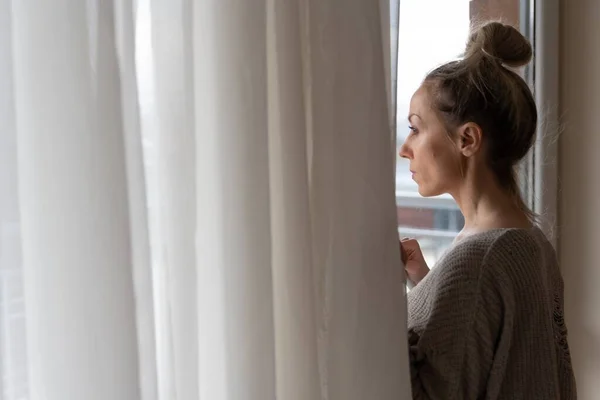 En ledsen kvinna tittar ut genom fönstret. Vinterdepression. — Stockfoto