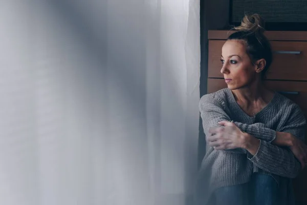 Hermosa mujer triste sentada en el suelo mirando a la ventana. — Foto de Stock