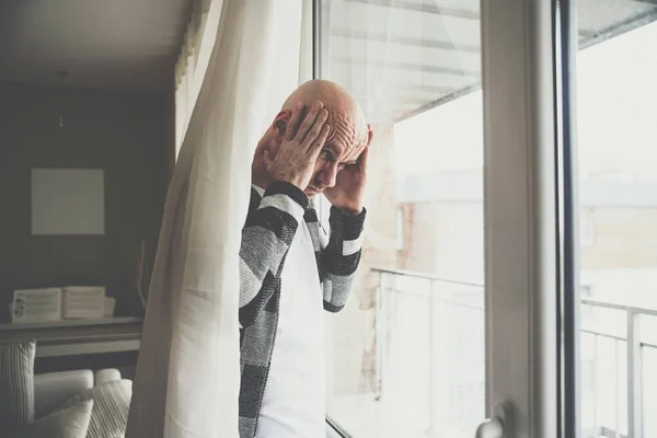 A worried man is standing by the window holding his head. — Stock Photo, Image