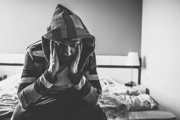 Un uomo depresso è seduto sul letto in camera da letto tenendo la testa. — Foto Stock