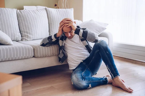 Un hombre preocupado está sentado en el suelo sosteniendo su cabeza. — Foto de Stock