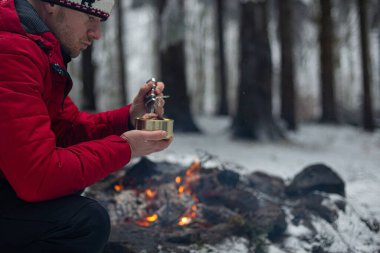 Ateşin yanında yakışıklı bir adam, dağ yolunda elinde konserve yiyeceklerle..