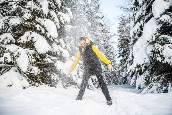 Vacker kvinna i hörselkåpor kastar snö en underbar vinterdag. Berg, vinterlandskap. — Stockfoto