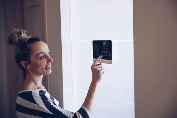 Blondine vrouw voert code in op het toetsenbord van alarmsysteem in het appartement. — Stockfoto