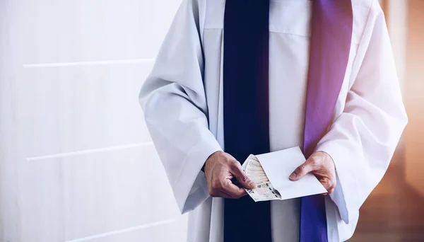 Catholic priest holding envelope with money during pastoral visit called kolenda in Poland