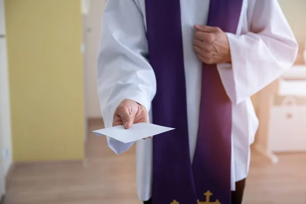 Prêtre catholique tenant une enveloppe avec de l'argent lors d'une visite pastorale appelée kolenda en Pologne — Photo