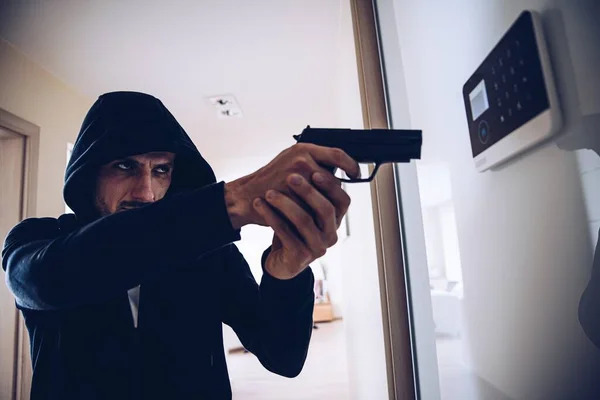 Een dief in een kap met een pistool breekt in het appartement in.. — Stockfoto