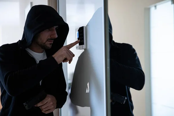 Ein Einbrecher mit einer Waffe in der Hand versucht, den Alarm zu entwaffnen. — Stockfoto