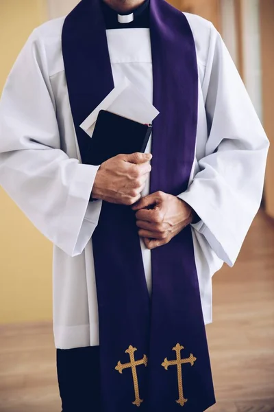 Um sacerdote segura um envelope com dinheiro na Bíblia Sagrada durante uma visita pastoral. — Fotografia de Stock