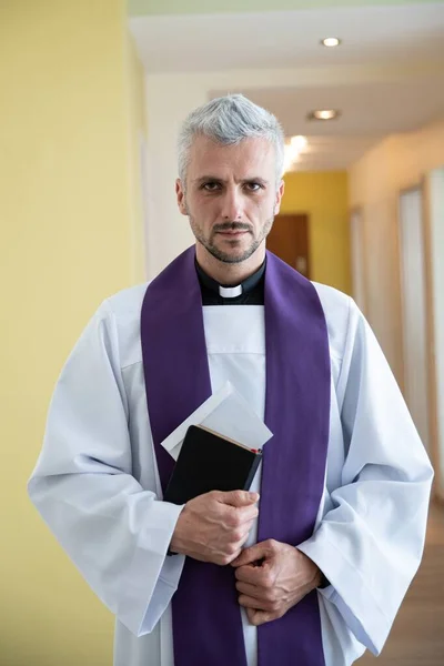 Ksiądz katolicki trzymający kopertę z pieniędzmi podczas wizyty duszpasterskiej. — Zdjęcie stockowe
