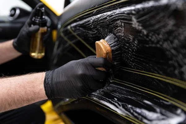 Pracownik myjni samochodowej czyszczący tapicerkę ze skóry szczotkowanej. — Zdjęcie stockowe