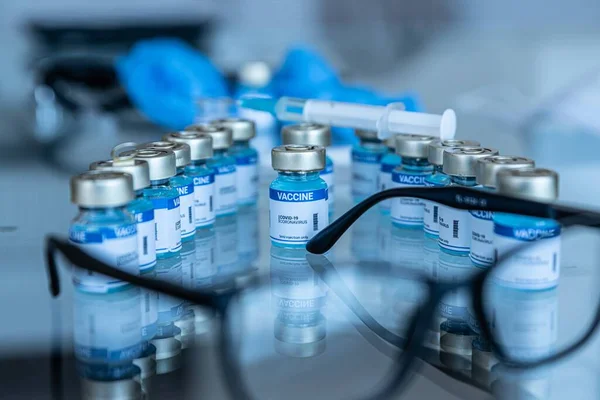 Ampollas con vacuna Covid-19 y jeringa con aguja en un banco de laboratorio. — Foto de Stock