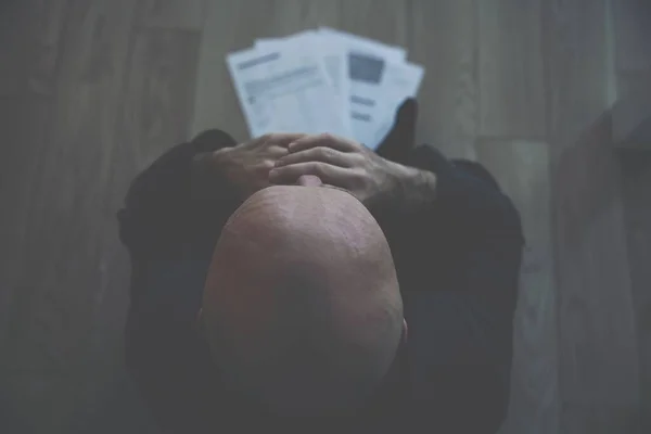 Ein trauriger und verzweifelter Mann sitzt auf dem Boden. Konkursunterlagen liegen auf dem Boden. — Stockfoto