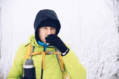 Kışlık ceketli yakışıklı adam sıcak çay içiyor..