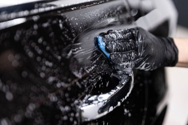 Araba yıkama işçisi araba boyasını kille temizliyor.